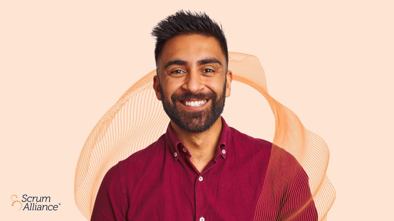 A professional man smiles in front of a branded Scrum Alliance background